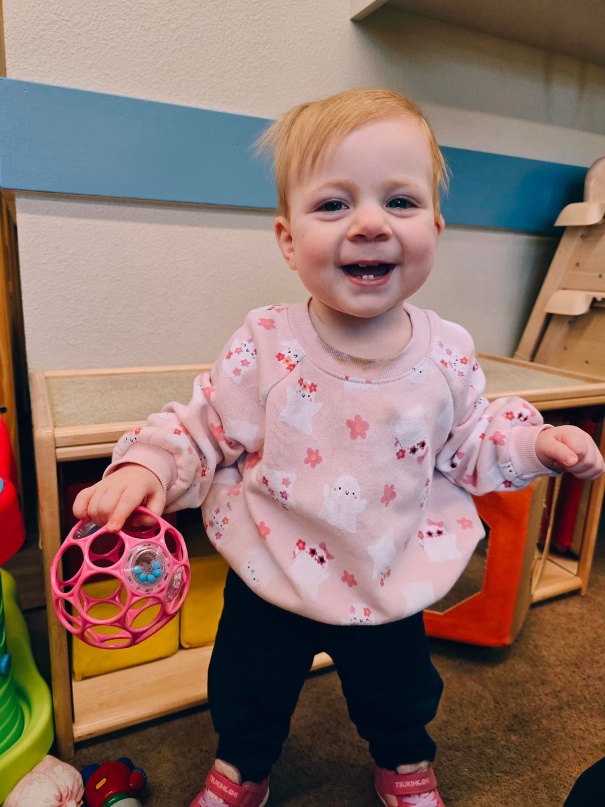 Smiling infant girl explores and learns through play with a pink ball at Primrose School in Keller, TX