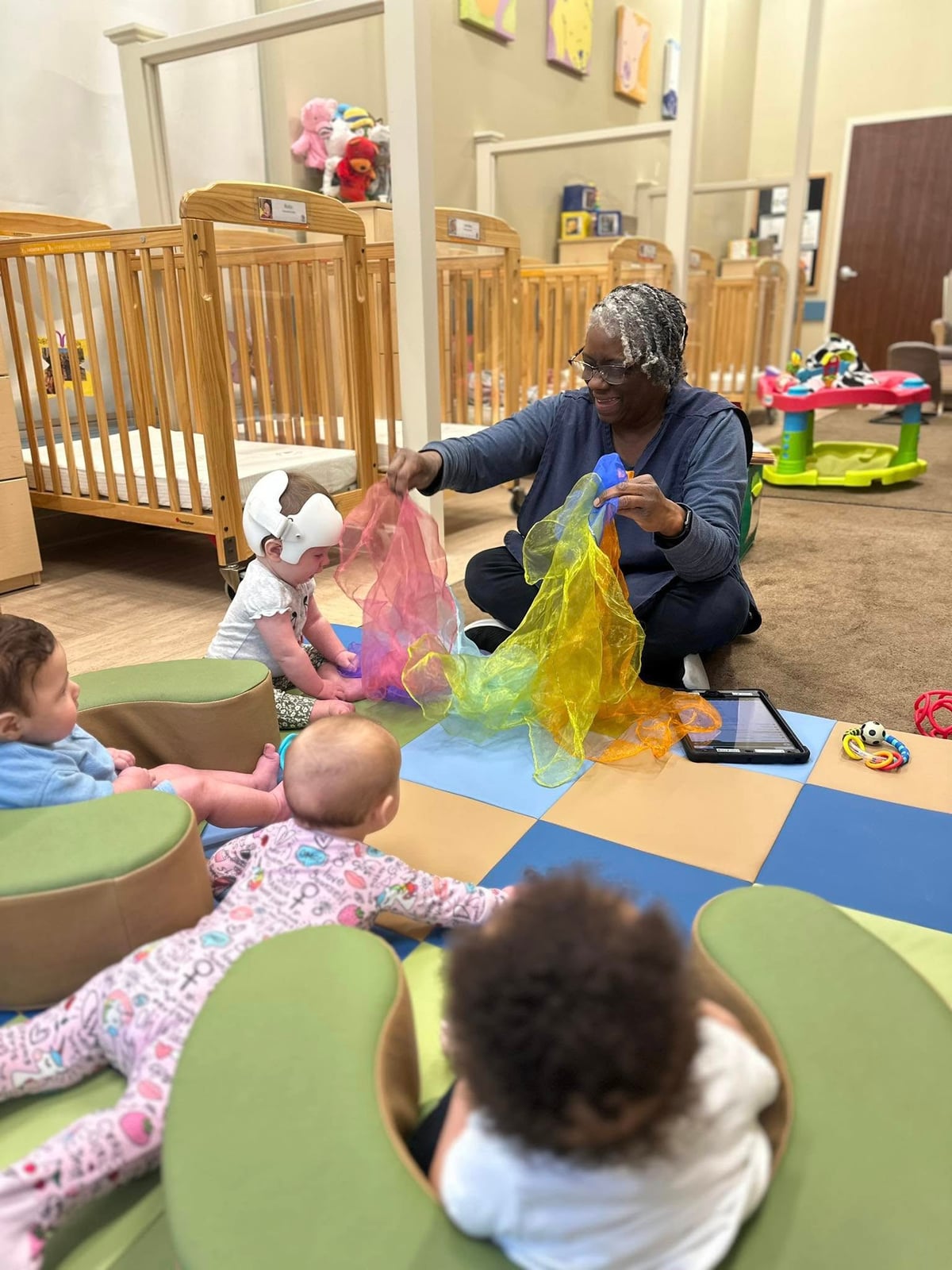 babies on a colorful playmat, engaging with their teaching holding colorful scarves
