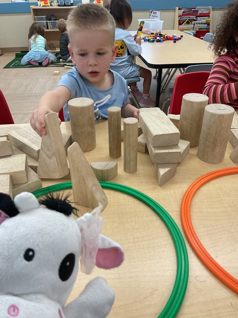 Preschool student exploring spatial awareness and problem-solving skills while building structures with wooden blocks during classroom center time.