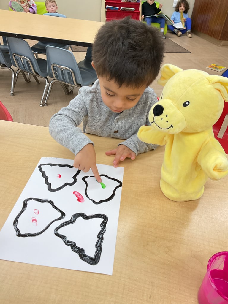 Preschool student using paint and finger tracing techniques to create artwork while developing fine motor skills and creativity.
