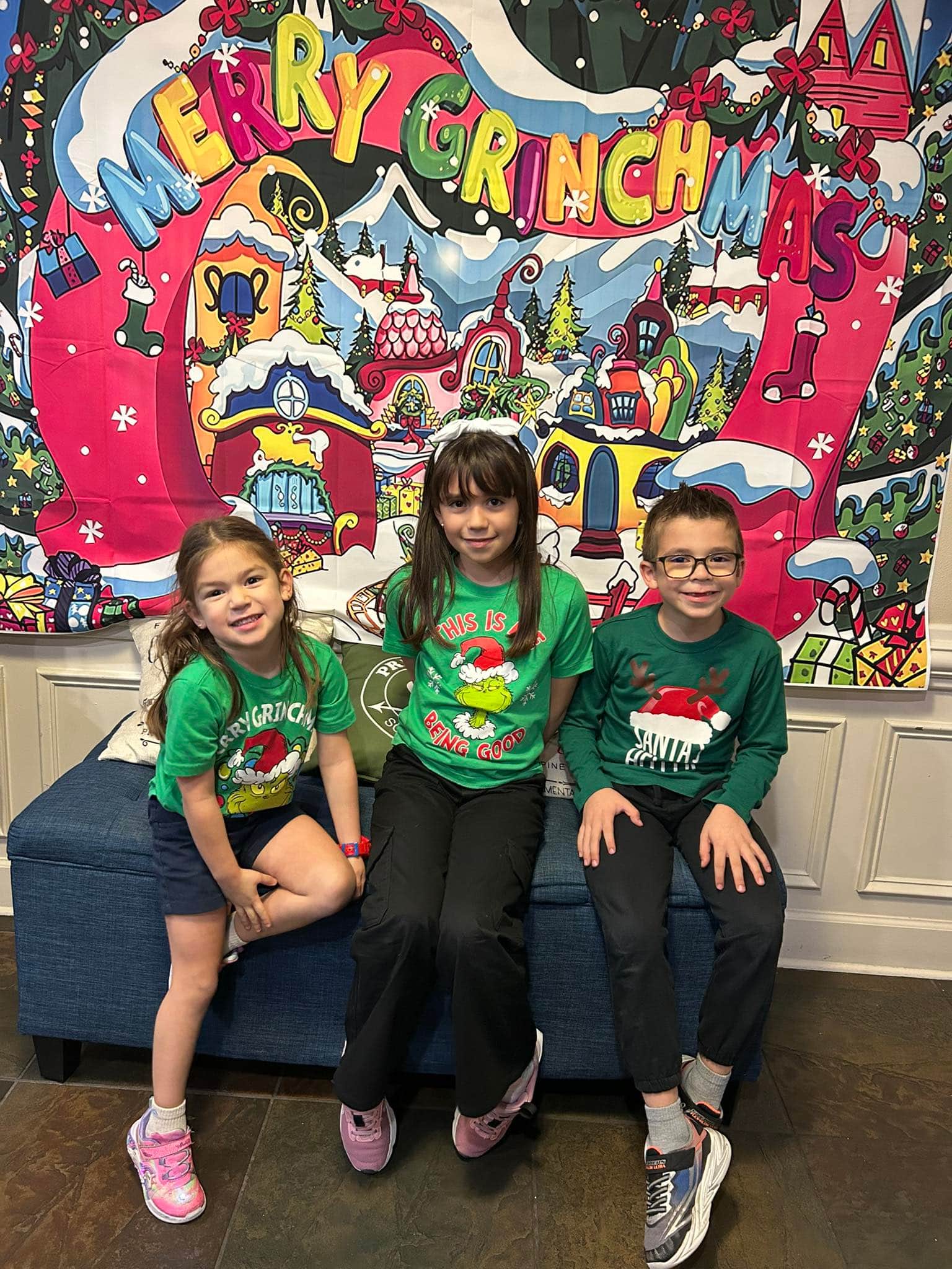 three children sitting on a bench in green shirts