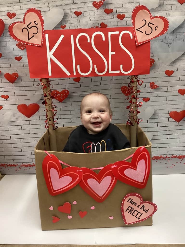 child sitting in box with hearts and it says kisses