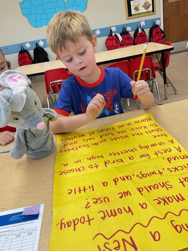 Preschool student practicing early writing and communication skills while creating a classroom project and sharing ideas with peers.