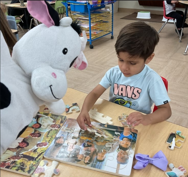Preschool student assembling a large family-themed puzzle while practicing critical thinking, spatial awareness, and fine motor skills.