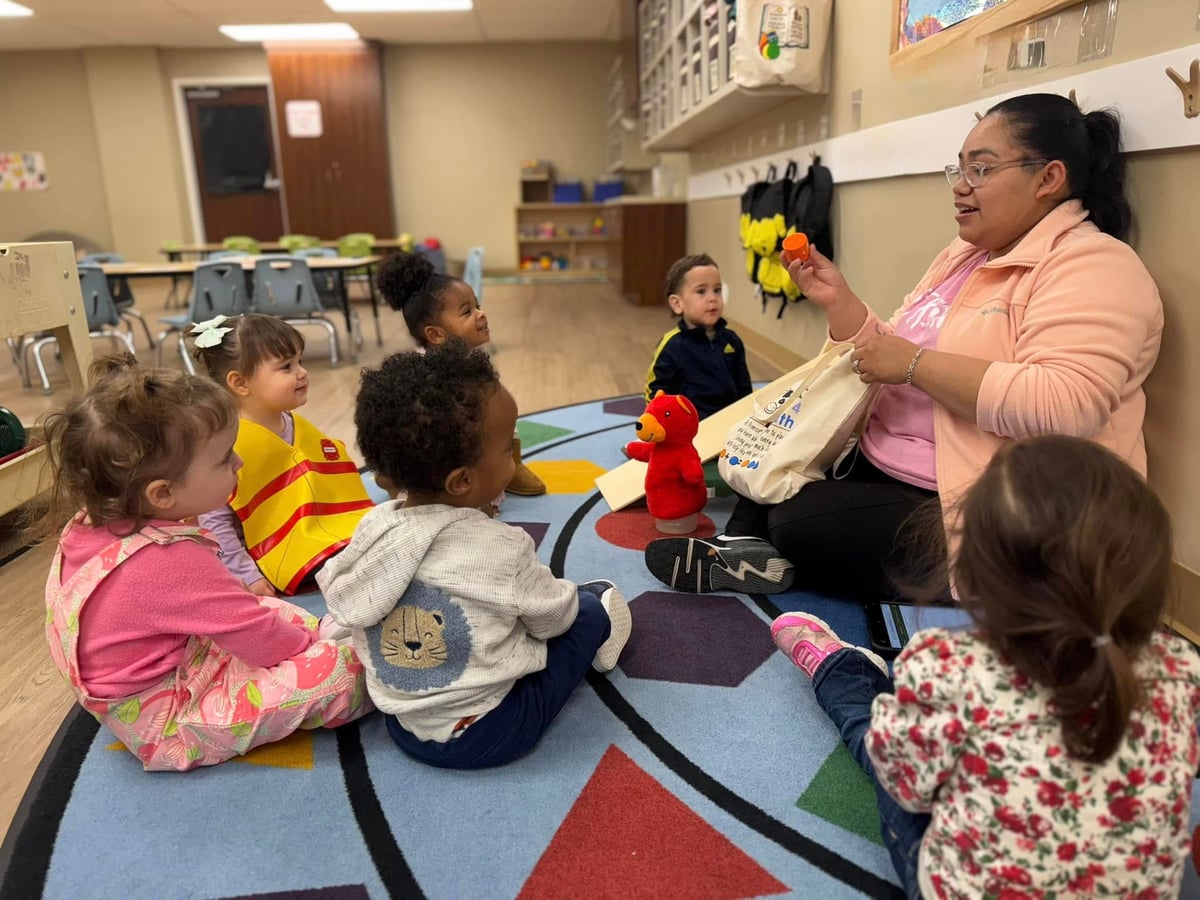 children sitting on a colorful carpet doing circle time with their teacher