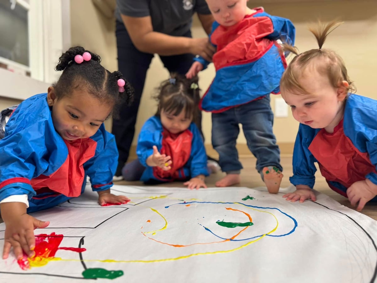 four children wearing smocks fingerpainting with a teacher