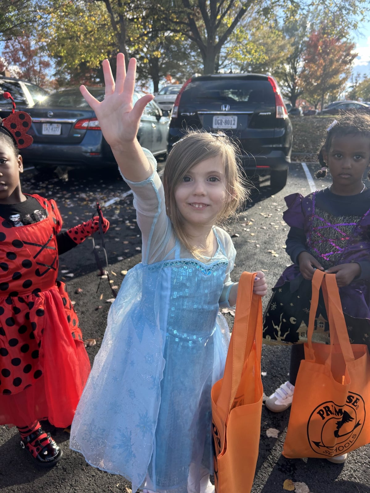Children dressed as witches and wizards enjoying a Trunk or Treat event at Primrose School with decorated cars, costumes, and families celebrating together.