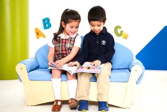 two children sitting on a couch reading together