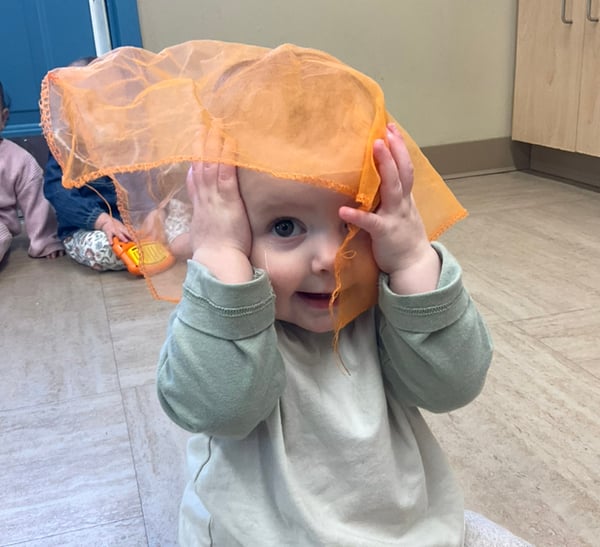 baby covering head with a scarf and smiling