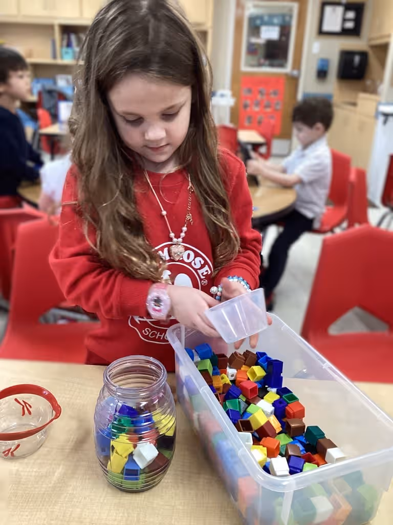 little girl placing colored cubes into a clear jar