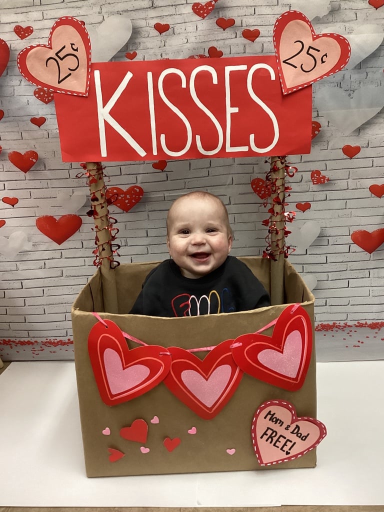 child sitting in box with hearts and it says kisses