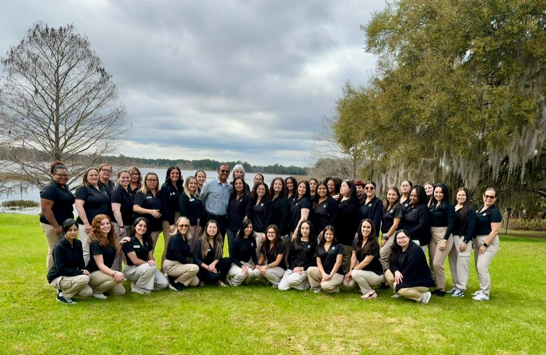 women in black polos and khaki pants on the grass in front of a lake