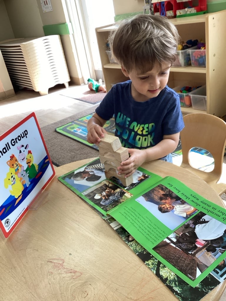 boy building with blocks on a table with a green book