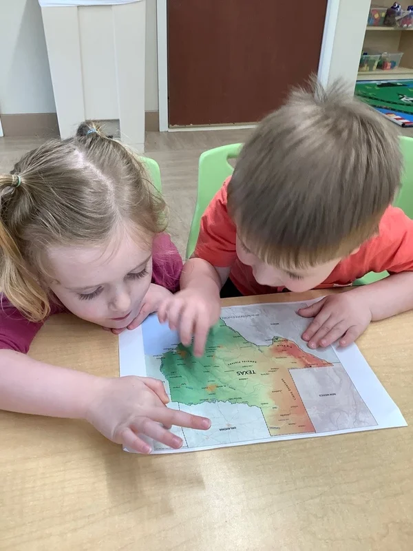 Two children happy and engaged as they learn about a map of Texas together during morning instruction.