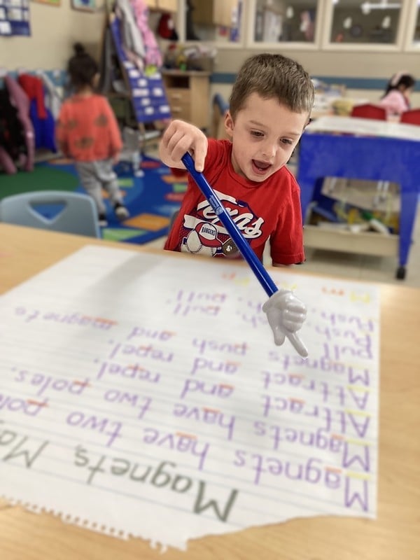 A little boy holding a pointer to words on a piece of paper