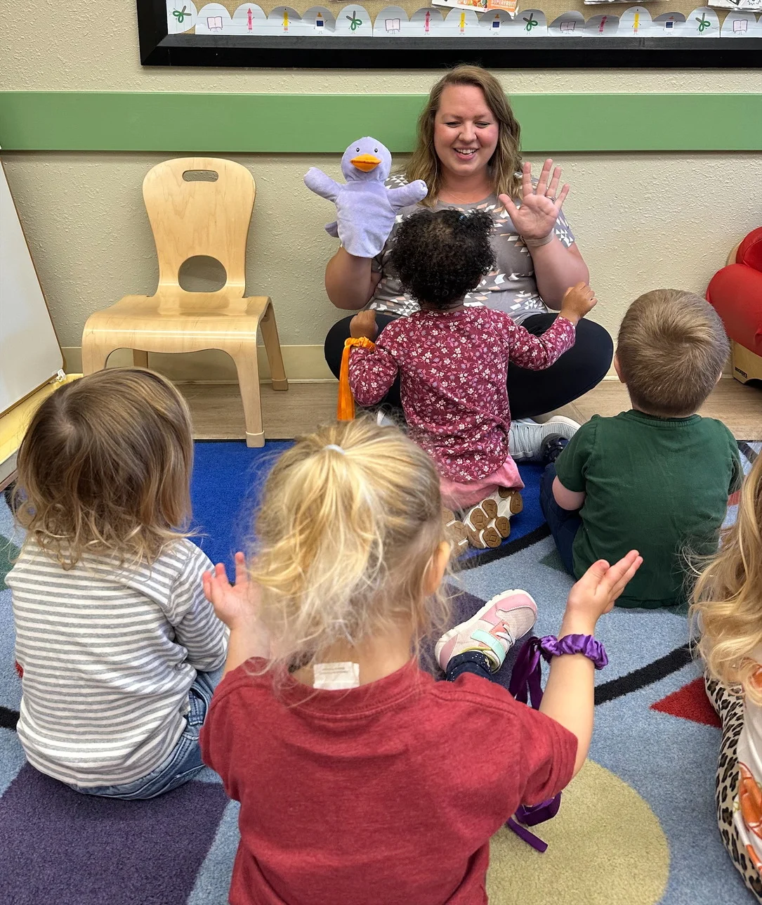 Vibrant Early Preschool Teacher at Primrose School of Eagan Leads a Captivated Group of Toddlers in Dynamic Classroom Instruction, Encouraging Exploration, Social Interaction, and Foundational Learning in a Joyful Early Childhood Space