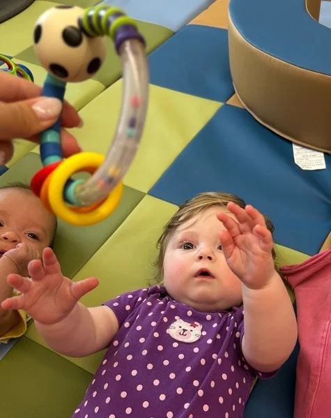 Infant reaching for a toy in the air and tracking it with her eyes.