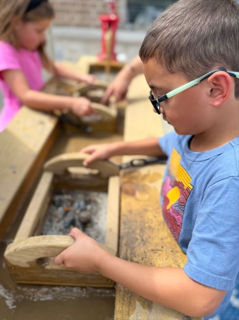 Children exploring wooden sifters in water to uncover hidden gems in dirt at the best summer camp in Haslet, TX.