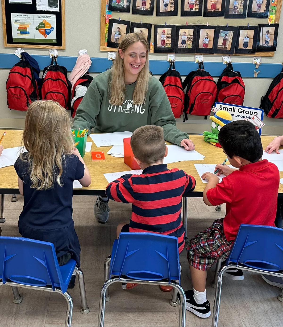Preschool teacher guiding three students during a writing table lesson plan at Primrose School of Eagan