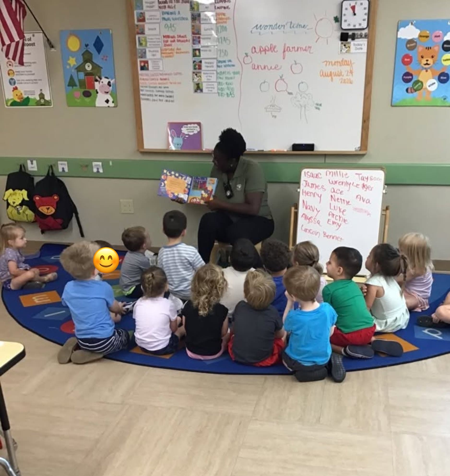 Children reading a book with a teacher at the carpet
