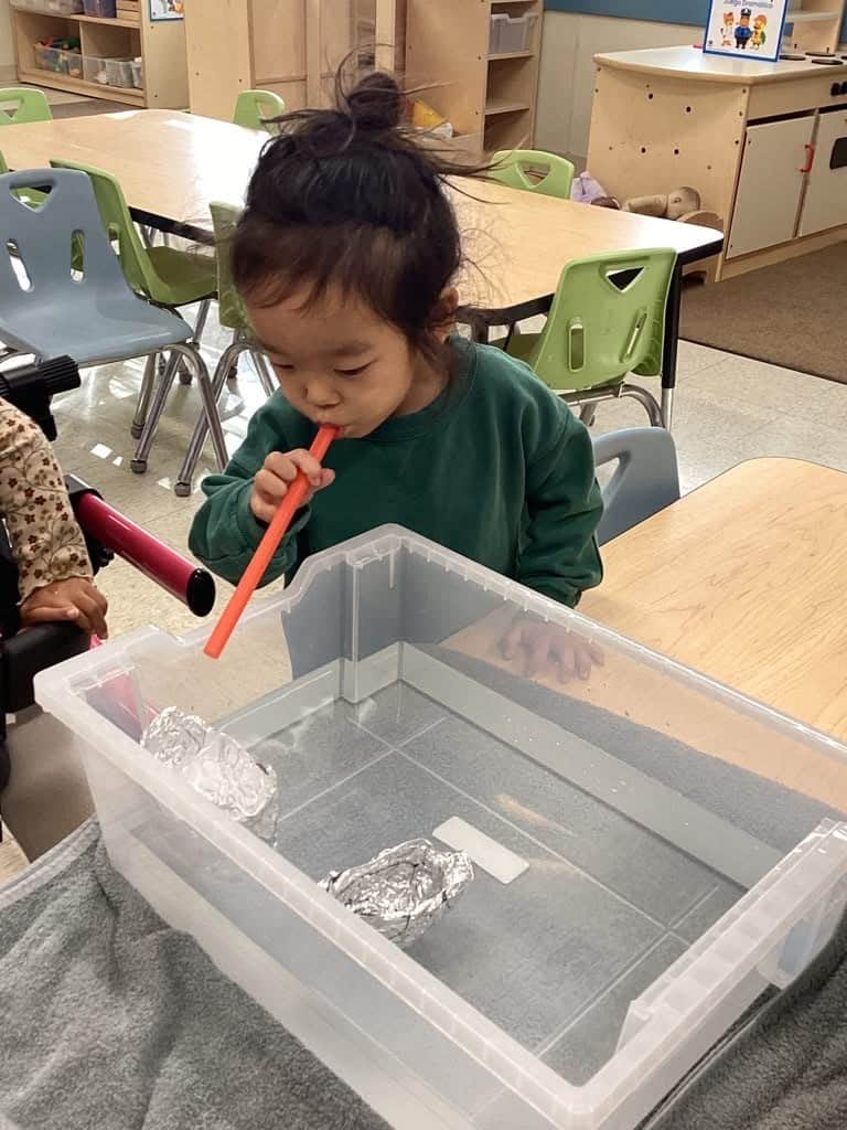 little boy blowing through a straw to move an aluminum boat in water.