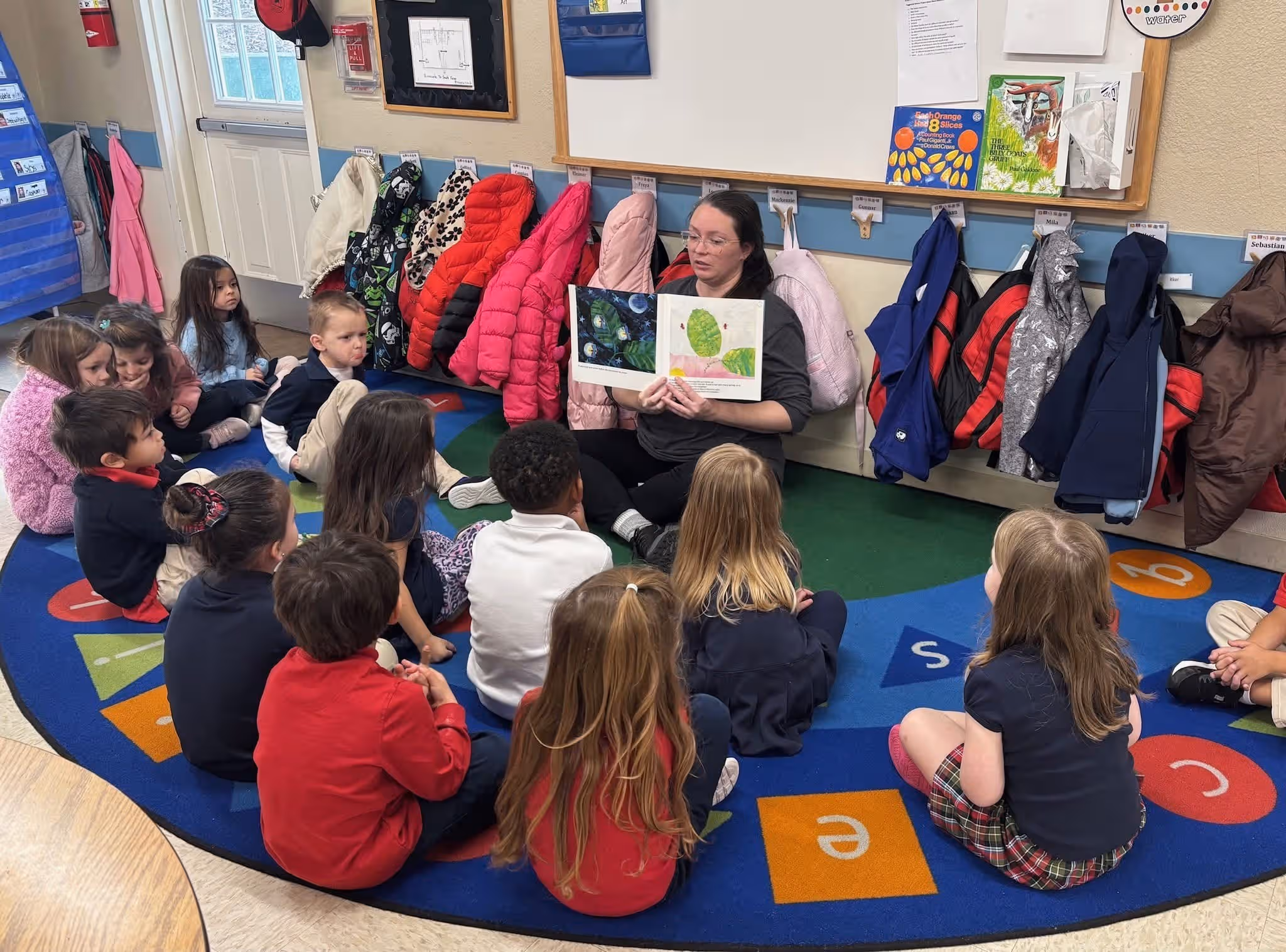 a group of children sitting on a carpet listening to a teacher read a book