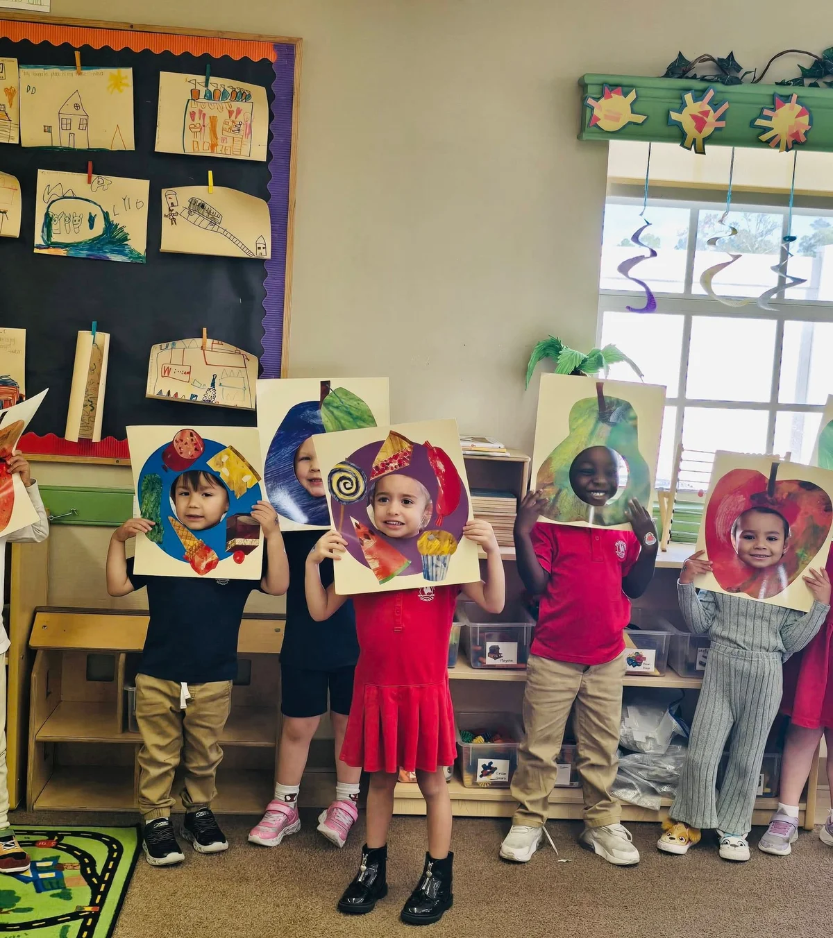 Children standing on a rug in a classroom holding different fruit cut outs