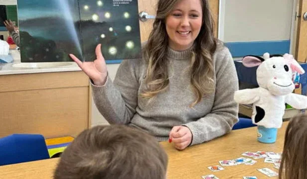 Teacher reading a science lesson book to a group of children at a classroom table at Primrose School of Eagan