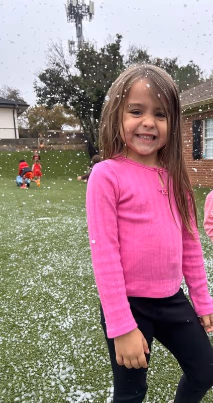 little girl in pink shirt on playground with fake snow falling