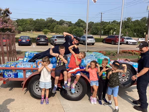 a trailer loaded with water bottles and sports drinks with firefighters and students posing in front
