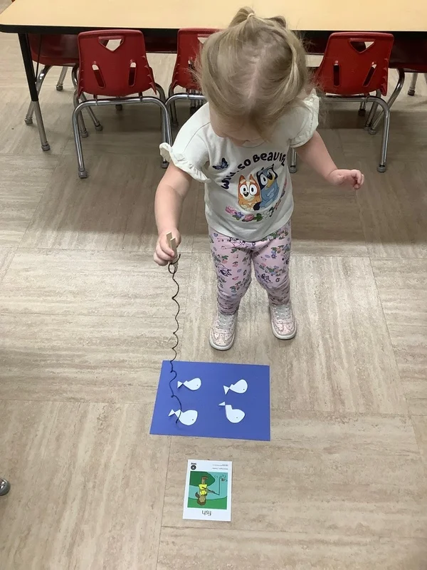 Young child participating in a preschool fishing game using a magnetic wand and paper lightbulb cutouts, enhancing coordination and early math skills at the best childcare in Alliance.