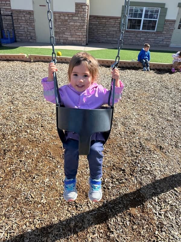 A child having fun swinging outside on the playground at Primrose school of north colorado springs