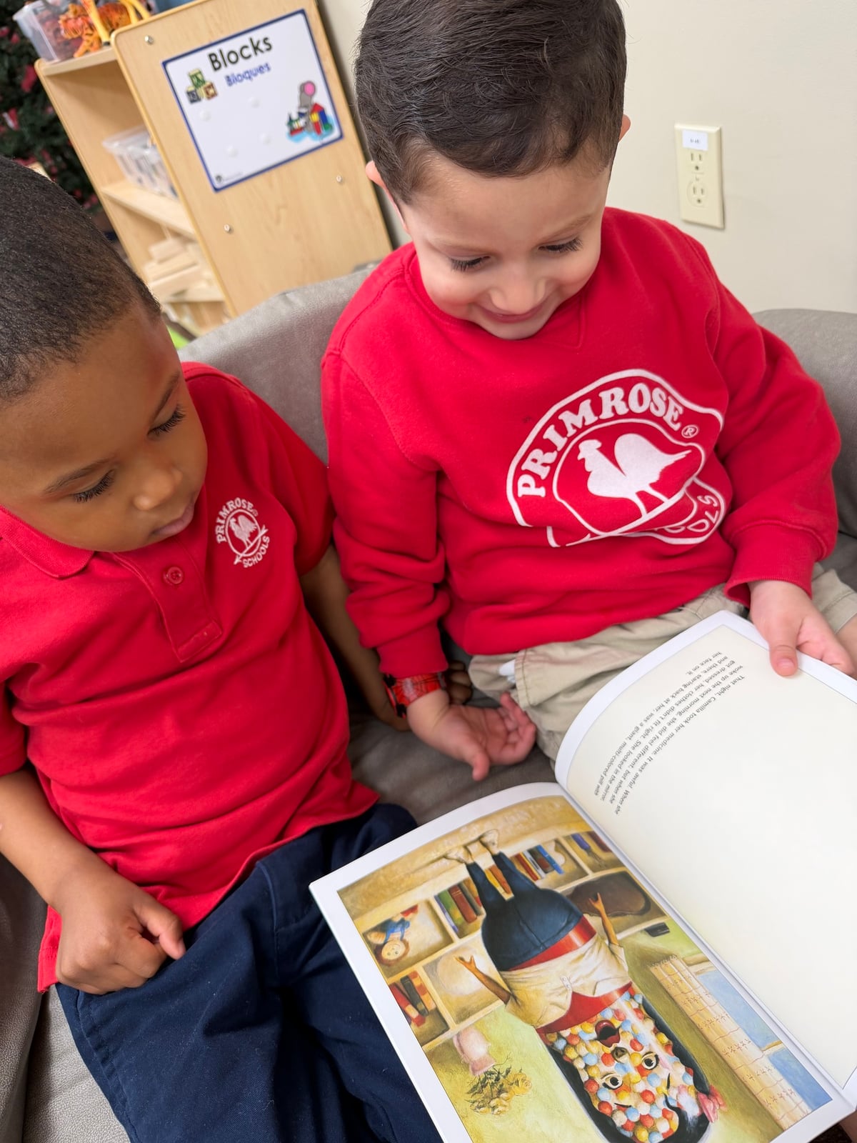 two boys in red shirts reading a book sitting on a bench